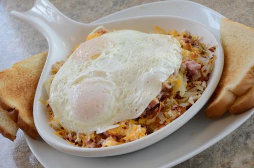 A dish of hash browns topped with cheese, ham, and two fried eggs, served with two slices of toasted bread.