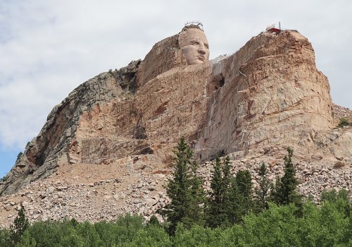 A large stone sculpture of a face carved into a mountain, surrounded by trees and rocky terrain under a cloudy sky.