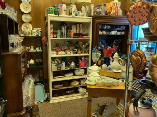 A cluttered room filled with various kitchenware, glassware, and collectibles on shelves and tables.