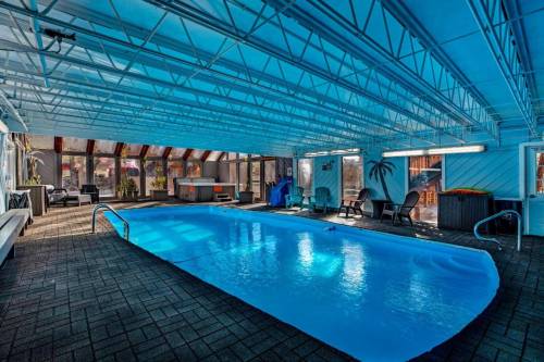 Indoor swimming pool with blue water, surrounded by lounge chairs and large windows, under a bright blue ceiling.