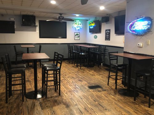 A spacious bar area with wooden floors, empty tables, and neon signs on the walls.