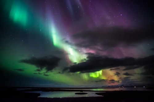 Vibrant auroras dance across a night sky filled with stars, casting colorful reflections over a tranquil landscape.