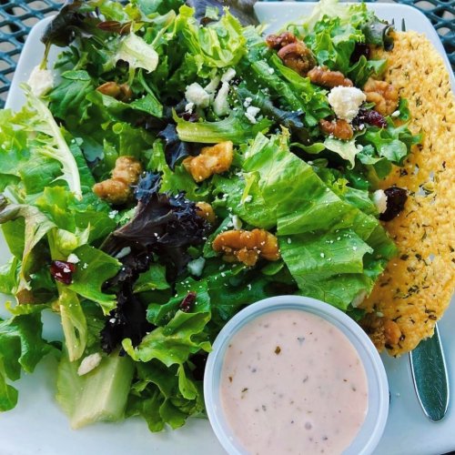 A fresh salad with mixed greens, walnuts, feta cheese, and a side of dressing on a white plate.