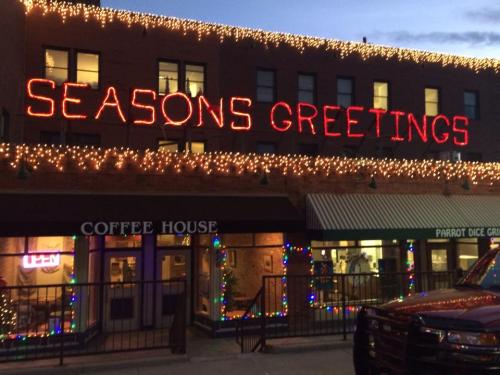 A building decorated with festive lights displays "SEASONS GREETINGS" above a coffee house and a dice game shop.