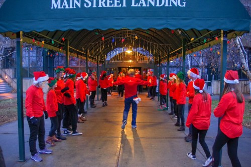 A group of people in red shirts and Santa hats gather under a festive canopy at Main Street Landing.