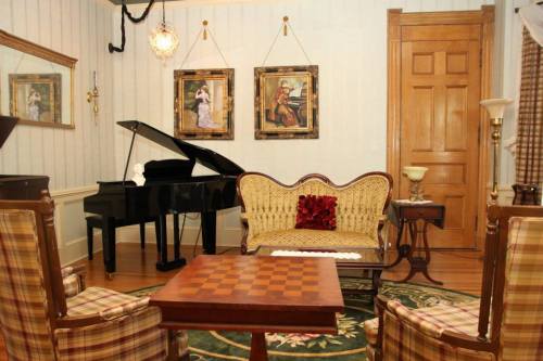 A vintage living room with a grand piano, elegant seating, a checkered table, and framed artwork on the walls.
