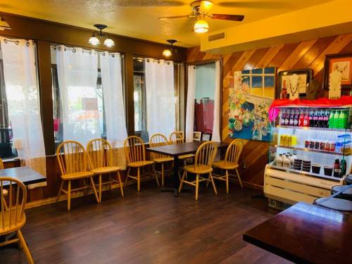 Cozy restaurant interior with wooden walls, empty tables, and a colorful drink fridge under bright lighting.