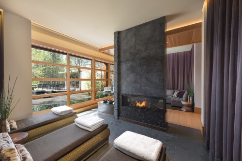 A serene spa interior featuring a modern fireplace, large windows, and cozy seating with towels neatly arranged.