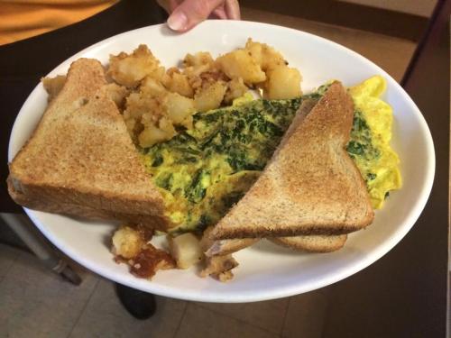 A plate with a spinach omelet, two slices of toast, and a serving of diced potatoes.