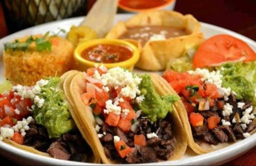 A plate of tacos filled with beef, guacamole, and pico de gallo, served with rice, beans, and salsa.