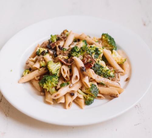 A plate of penne pasta with broccoli, mushrooms, and a creamy sauce, garnished with seeds.