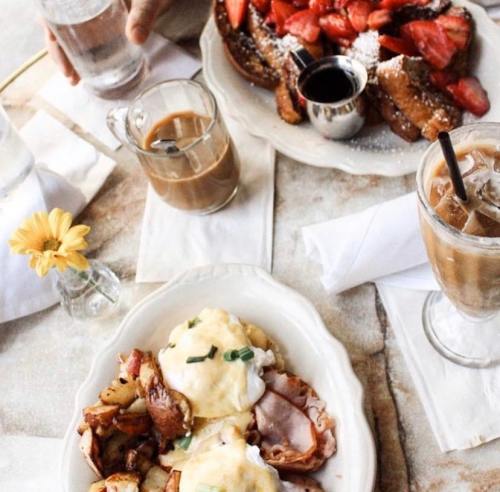A table set with two plates of brunch: eggs Benedict with potatoes and French toast topped with strawberries and syrup.