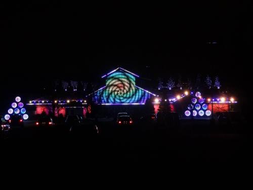 A brightly lit house at night, decorated with colorful lights and patterns, surrounded by illuminated trees and vehicles.