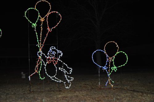 Two illuminated bear figures holding colorful balloons, set against a dark night background.