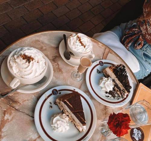 Three desserts on a table: two cups of whipped cream and two plates of layered cake, with a small glass of liqueur.