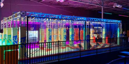 A colorful indoor obstacle course with climbing structures and ropes, illuminated by vibrant lights.