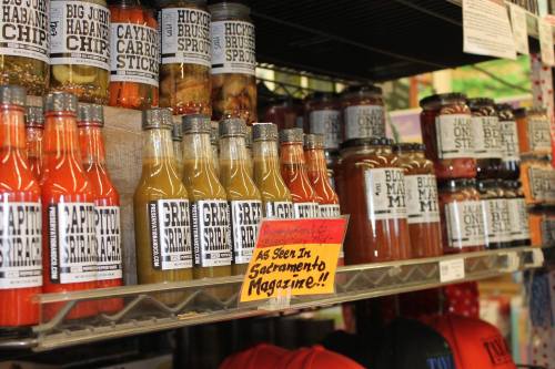 Shelves filled with various snacks and sauces, including chips and bottles, with a sign reading "As Seen in Sacramento Magazine!"