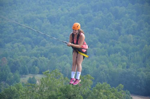 A girl in a helmet and harness zip-lining over a lush green landscape, focused on her descent.