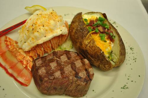 A plate featuring a grilled steak, lobster tail, and a loaded baked potato with cheese and green onions.