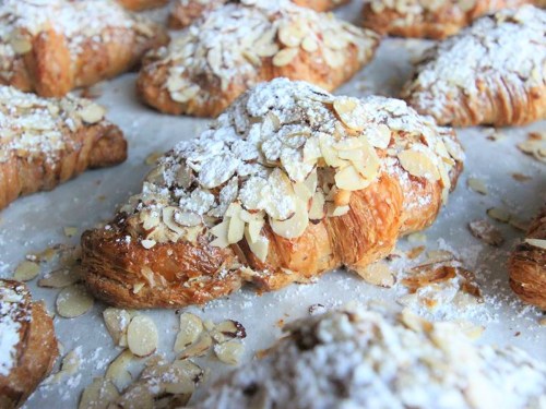 Freshly baked croissants topped with sliced almonds and powdered sugar, arranged on parchment paper.