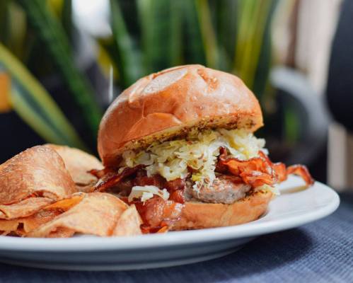 A close-up of a burger with bacon and sauerkraut, served with crispy potato chips on a white plate.