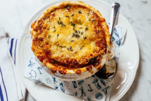 A bowl of French onion soup topped with melted cheese and herbs, served on a decorative plate with a spoon.