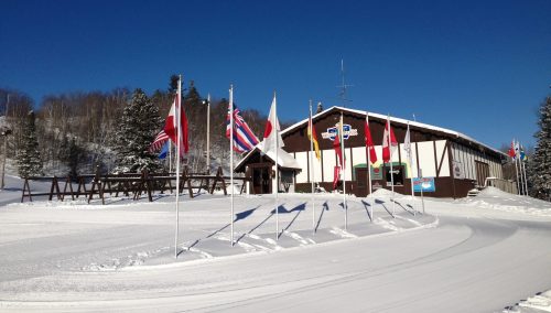 A snow-covered building surrounded by flags from various countries under a clear blue sky.
