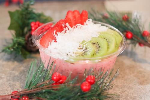 A colorful fruit bowl with strawberries, kiwi, and shredded coconut, surrounded by festive greenery and red berries.
