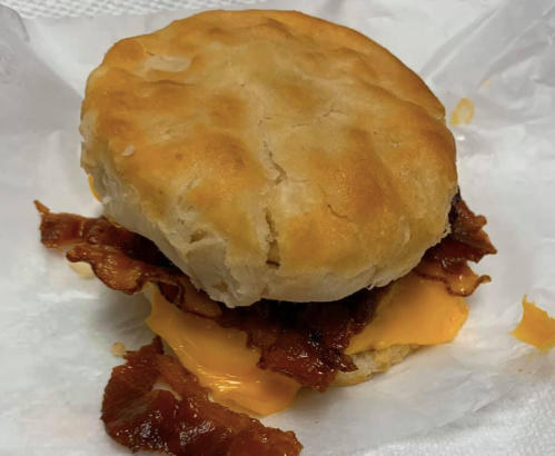 A biscuit sandwich with crispy bacon and melted cheddar cheese, served in a white wrapper.