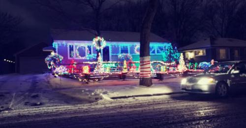 A house decorated with colorful Christmas lights, surrounded by snow, with a car parked on the street nearby.