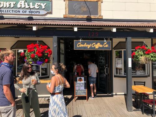 A group of people outside Cowboy's Coffee Co. with vibrant flower baskets and a sign, enjoying a sunny day.