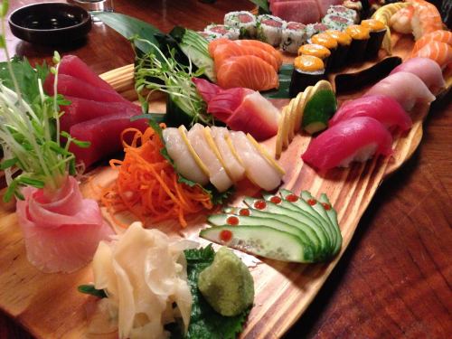 A beautifully arranged sushi platter featuring various types of sashimi, rolls, and garnishes on a wooden board.