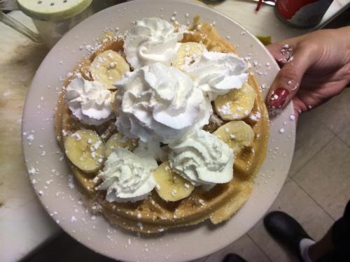 A plate of waffles topped with banana slices and whipped cream, dusted with powdered sugar.