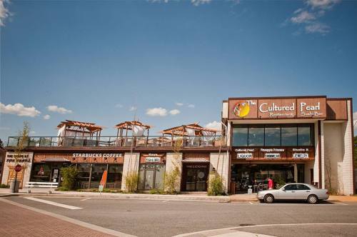 Exterior view of The Cultured Pearl restaurant and Starbucks, featuring outdoor seating and a clear blue sky.