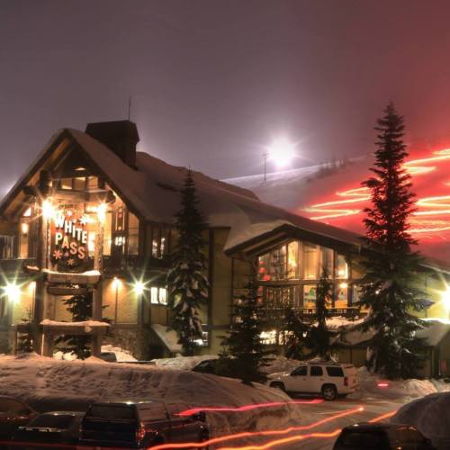 A cozy lodge at night, surrounded by snow, with ski trails illuminated in the background.