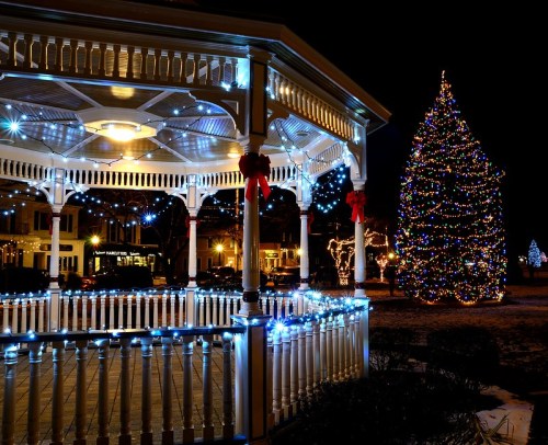 A beautifully lit gazebo at night, adorned with festive lights, next to a colorful Christmas tree.