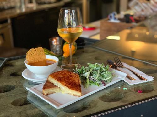 A gourmet grilled cheese sandwich with tomato soup, a side salad, and a glass of white wine on a restaurant table.