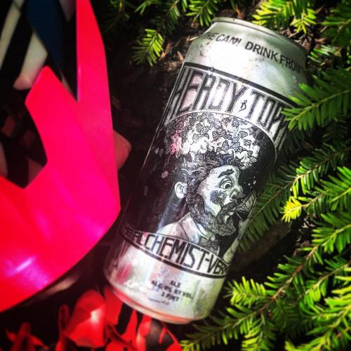 A can of Hedy Topper beer lies on green foliage, featuring a whimsical black-and-white design of a bearded man.