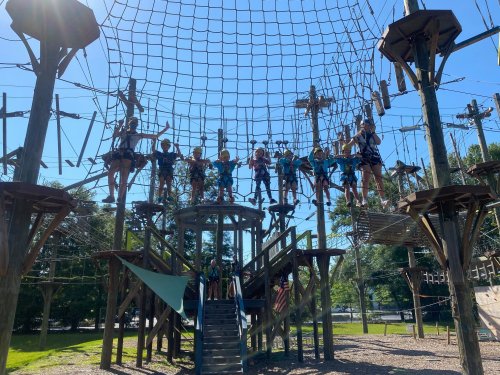 A group of people in harnesses navigating a high ropes course with nets and wooden structures on a sunny day.