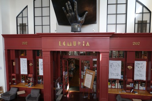 Interior of a library named "Lemuria," featuring a large hand sculpture and bookshelves with artwork on the walls.
