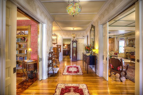 A beautifully decorated hallway with wooden floors, vintage furniture, and colorful rugs leading to various rooms.