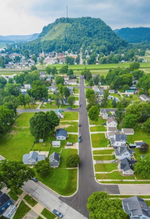 Aerial view of a small town with green hills, tree-lined streets, and residential homes.