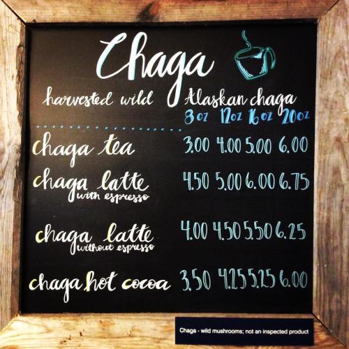 Chalkboard menu displaying prices for Alaskan chaga tea, latte, and hot cocoa in various sizes.