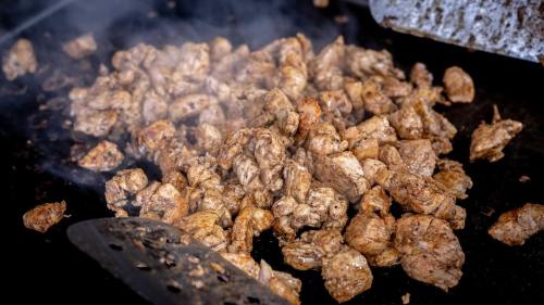 Sizzling pieces of seasoned meat cooking on a grill, surrounded by steam and smoke.