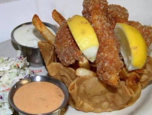A plate featuring crispy fish fillets with lemon, fries, and coleslaw, served in a tortilla bowl with dipping sauces.