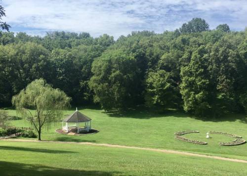 A serene park scene featuring a gazebo surrounded by lush greenery and flower beds on a sunny day.