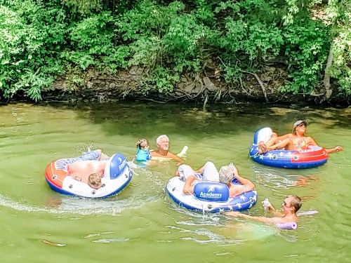 A group of people floating on colorful inner tubes in a green river, enjoying a sunny day.