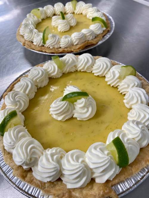 Two lime pies with whipped cream and lime slices, arranged in decorative patterns on a silver surface.