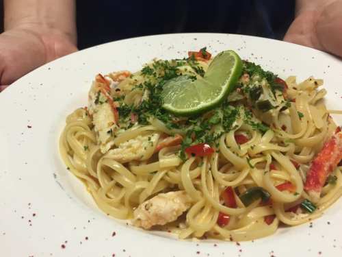 A plate of pasta with crab, lime, and herbs, garnished with red pepper flakes, held by hands.