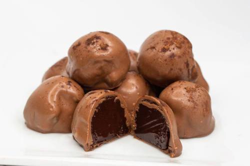 A pile of chocolate truffles, some whole and one cut in half, revealing a rich, dark chocolate filling.